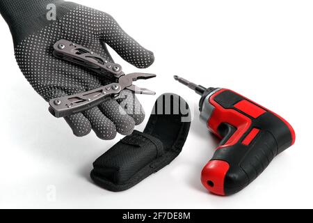 A man disassembles folding pliers. In the background is an electric screwdriver. Multi-tool. A home tool for small home repairs Stock Photo