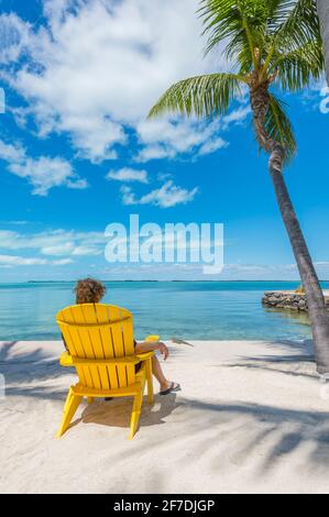 Woman sitting in yellow adirondack chair, staring out contemplatively at Caribbean ocean on incredibly beautiful sunny day.