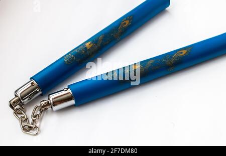 Closeup of karate sticks, or nunchuks, held together by a metal chain and decorated with gold dragons on blue protective foam. Stock Photo