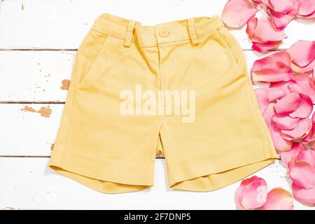 Yellow shorts on a white wood and some rose petals.The photograph is an overhead shot with a horizontal format. Stock Photo