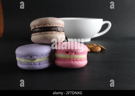 French dessert cuisine three macaroons lie pyramid to lies almonds and a cup of coffee in the background on a black background with a copyspace . Stock Photo