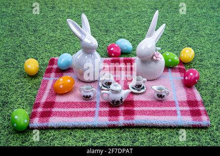 Decoration with ceramic Easter bunnies in the meadow with the teacups, teapots and Easter eggs. Template for Easter greeting card, postcard, poster. Stock Photo