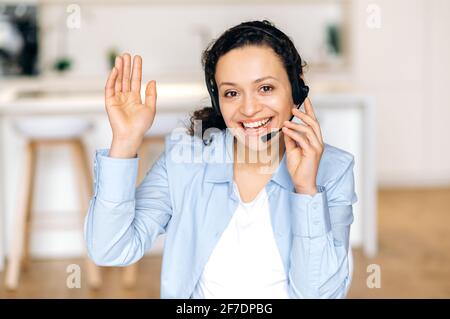 Front view headshot of confident friendly mixed race woman, freelancer or call center operator, agent or expert, with headset, communicating with client or employee through headphones, smiles friendly Stock Photo