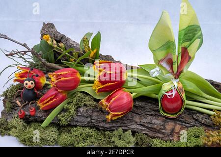 Decoration for Easter, tree bark adorned with tulips, colored egg, cockchafer toys. Template for Easter greetings, postcards. Stock Photo