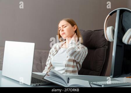 Young woman suffers from neck pain. Tired woman have headache and cervical back pain while sitting working in office or at home workspace. Teenager gi Stock Photo