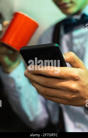 selective focus of a mobile phone used by a young man to send messages over the internet before going to work and having breakfast with a cup of coffe Stock Photo