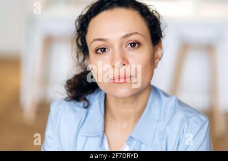 Close-up portrait of serious successful confident beautiful brunette mixed race business lady, in blue formal shirt, looking at camera Stock Photo