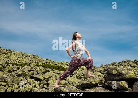 Young woman practicing balance yoga exercises on a sunny day under the sky on a mountain top. Summer vacations outdoor harmony and healthy life Stock Photo