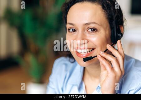 Close-up headshot of confident friendly mixed race woman, freelancer or call center operator, agent or expert, with headset, communicating with client or employee through headphones, smiling friendly Stock Photo