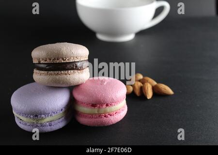 French dessert cuisine three macaroons lie pyramid to lies almonds and a cup of coffee in the background on a black background with a copyspace . Stock Photo