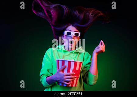 Photo of funky scared young woman dressed green pullover visiting cinema eating pop corn isolated vivid vibrant dark abstract background Stock Photo