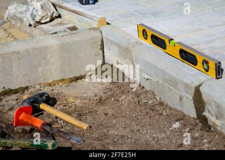 Defocus Paving Backyard Patio. Yellow spirit level, hammer, mallet, chisel and lie on the ground. Set of tools for laying paving stones. Cement curbs. Stock Photo
