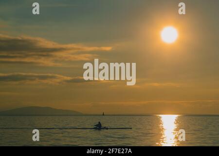 Kayaker or a person in a paddle boat on a lake during evening hours. Romantic leisure activity on the water. Sun about to set into the water. Stock Photo