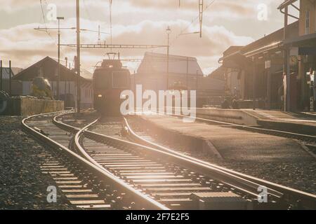 Train station in switzerland, frontal view of the train and train tracks in strong evening sunset light. Typical branch line station in Switzerland. Stock Photo