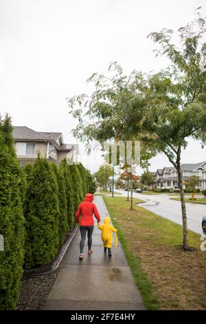 Rear view of mother walking with toddler child on the sidewalk. Stock Photo