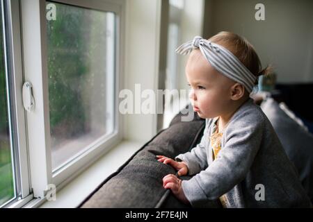 Pretty young girl looking out window from inside her home. Stock Photo