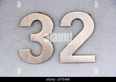 Number 32 in stainless steel on a white plaster wall Stock Photo