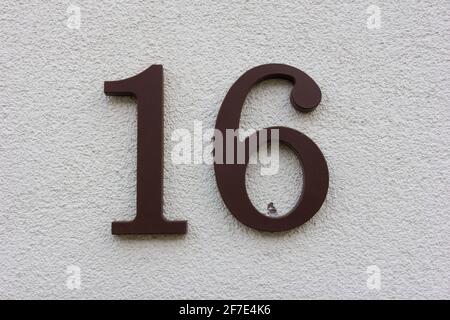 Number 16 in brown plastic on a white plaster wall Stock Photo