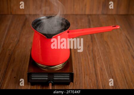 Small mobile electric single plate cooker with a red coffee pot on it. Steam or smoke is rising from the pot while making coffee or other hot beverage Stock Photo