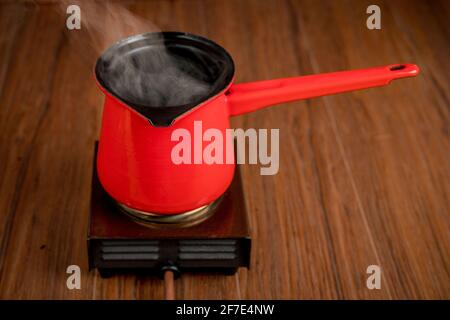 Small mobile electric single plate cooker with a red coffee pot on it. Steam or smoke is rising from the pot while making coffee or other hot beverage Stock Photo