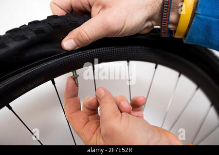 Bicycle repair - a person is inserting a washer on a presta valve on a carbon bicycle rim and tire. Finger pointing towards the valve. Stock Photo