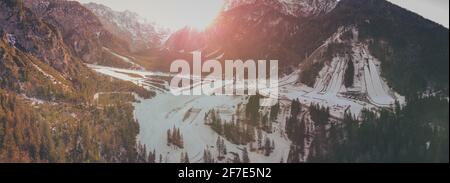 Panoramic photo of Planica and ski jumping hills in valley of Tamar, Slovenia, on a cloudy winter morning with sun just at the edge of photo. Valley c Stock Photo