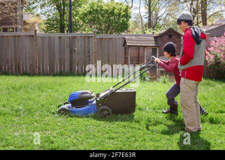 A boy mows lawn in early spring while father watches over him Stock Photo