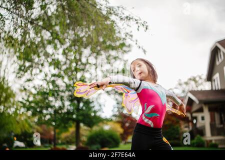 A little girl plays outside in butterfly wings with arms outstretched Stock Photo