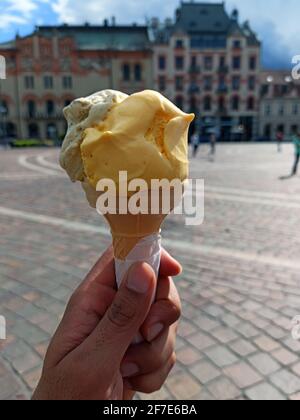 Close up of hand holding a delicious looking Saffron and coffee ice cream cone in front of European building exterior located in the center of Krakow, Stock Photo