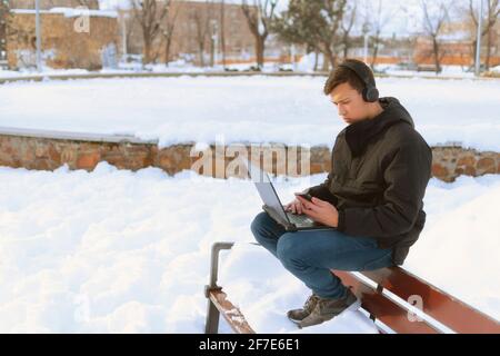 Millennial college boy studying on laptop with headphones in park Stock Photo