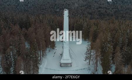 Aerial drone view of old deserted or abandoned famous ski jumping hill in Cortina d'Ampezzo, Italy on a winter day with snow.  Visible snowy forest in Stock Photo