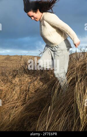 Woman Running Down Hill With Tall Grass As The Wind Blows in Denmark Stock Photo