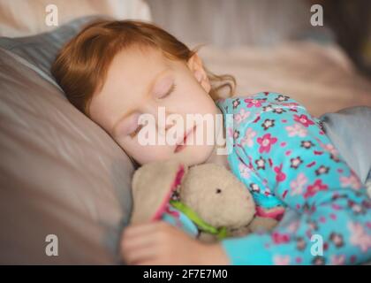 Sweet little red haired girl sleeping with stuffed bunny. Stock Photo