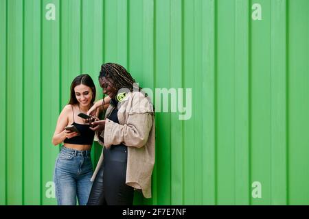 Two young multiethnic women talk, smile and look at their phones Stock Photo