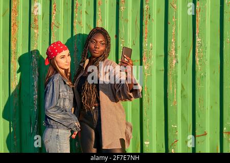 Two multiethnic women in urban clothing take a photo with a phone Stock Photo