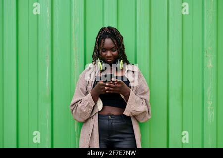 Black woman in urban clothing looks at her mobile while she is smiling Stock Photo