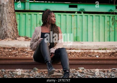 Black woman in urban clothing is sitting on abandoned train tracks Stock Photo