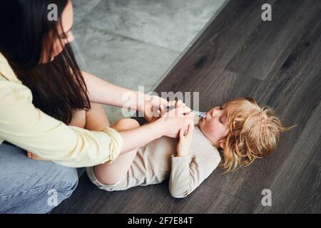 woman feeding baby food to her son, who is lying on the floor Stock Photo