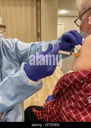 Elderly man receives Covid-19 vaccination from healthcare worker dressed in protective gear. Stock Photo