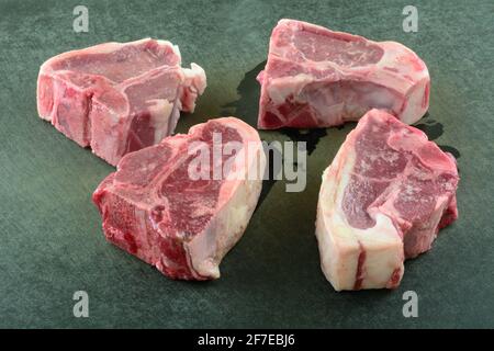 Closeup of four fresh raw lamb chops on black cutting board Stock Photo