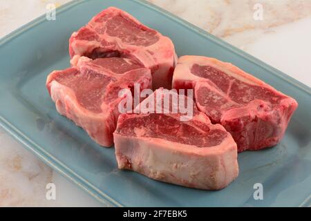 Four raw lamb chops on blue plate in preparation for grilling roasting or baking Stock Photo