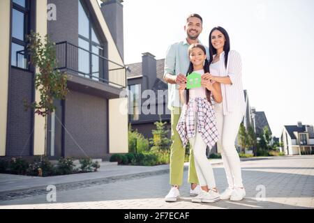 Full length photo of positive adorable family hands hold paper house card toothy smile look camera spend time outdoors Stock Photo