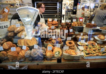 Baked goods for sale inside Tatte Bakery & Cafe with a female store worker behind.Harvard Square.Cambridge.Massachusetts.USA Stock Photo