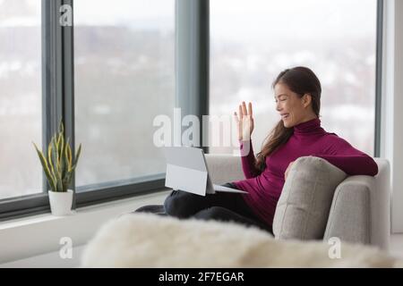 Work from home happy Asian woman remote working on laptop computer waving hello to coworkers on videocall teamwork during lockdown of coronavirus Stock Photo