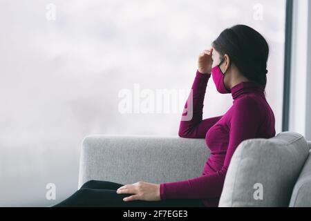 Coronavirus lockdown worried young woman wearing face mask sitting at home thinking about the pandemic and the consequences on the econoy. Anxiety Stock Photo