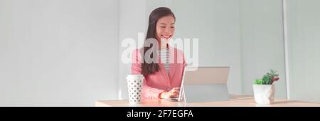 Working from home office Asian business woman using laptop for videocall or banking financial services wearing professional suit for live stream Stock Photo