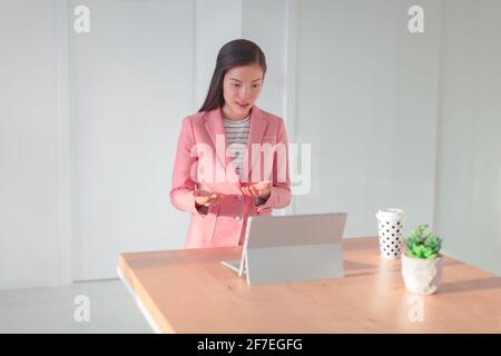 Videoconference online presentation Asian business woman talking teaching live webinar from home office streaming from laptop on standing desk Stock Photo