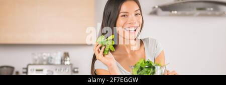 Vegetable cooking healthy diet woman eating spinach leaves at home banner panoramic. Smiling Asian girl happy making green juice recipe.