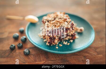 Blueberry fruit crumble. Sweet dessert homemade at home on blue plate and golden spoon on wooden table with fresh blueberries. Stock Photo