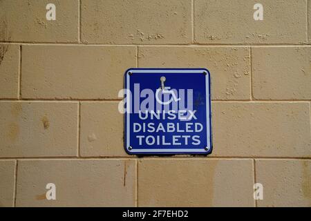 Unisex disabled toilets signage in blue and white on yellow brick wall Stock Photo
